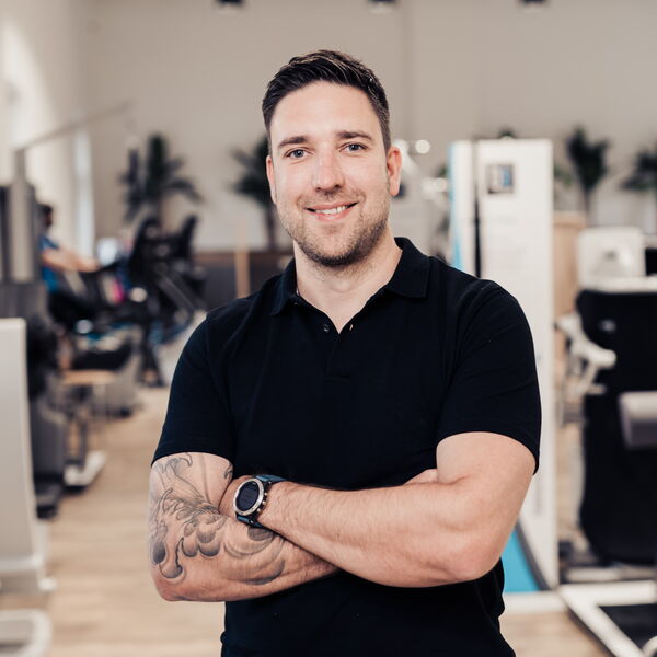 Ein lächelnder Mann mit Tattoos steht in einem modernen Fitnessstudio in Bochum-Mitte und posiert selbstbewusst.