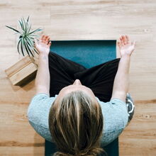 Eine Person meditiert auf einer Yogamatte, umgeben von Pflanzen, und fördert Fitness und Entspannung in Bochum.