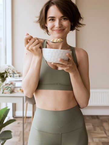 Eine junge Frau in Sportbekleidung lächelt, während sie in Bochum eine Schüssel gesunder Snacks genießt.