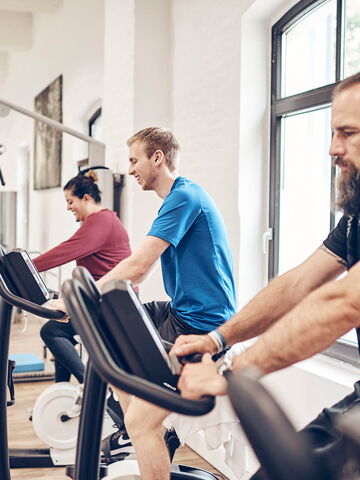 Drei Personen trainieren an Crosstrainern in einem modernen Fitnessstudio mit Helligkeit und angenehmer Atmosphäre.