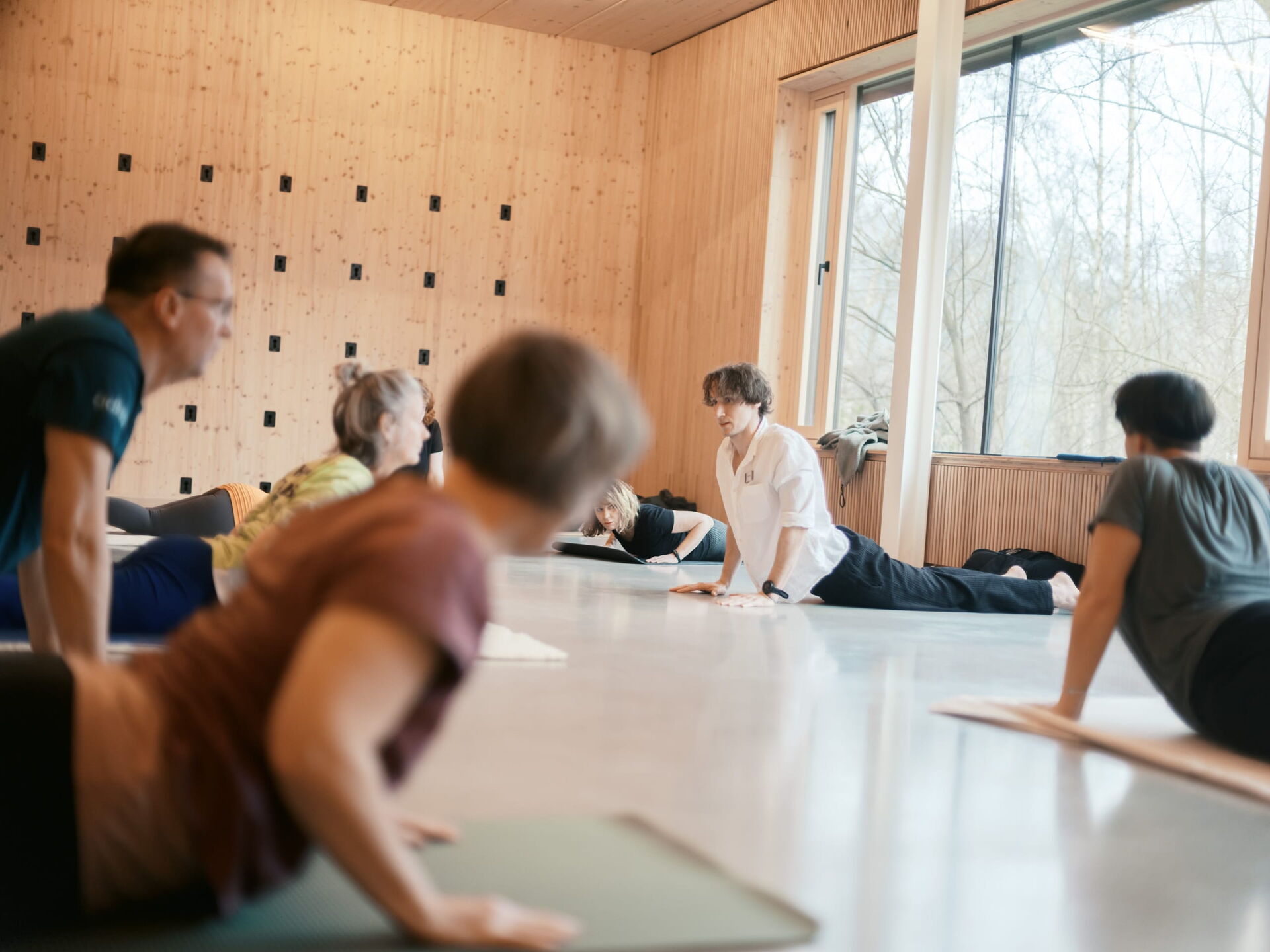 Eine Gruppe von Menschen nimmt an einer Yogastunde in einem hellen, modernen Raum mit großen Fenstern teil.