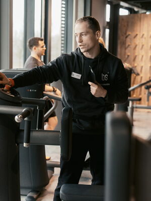 Ein Fitnessinstruktor erklärt einem Besucher die Bedienung eines modernen Trainingsgeräts im Fitnessstudio.