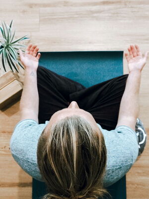 Eine Person meditiert auf einer Yogamatte, umgeben von Pflanzen, und fördert Fitness und Entspannung in Bochum.