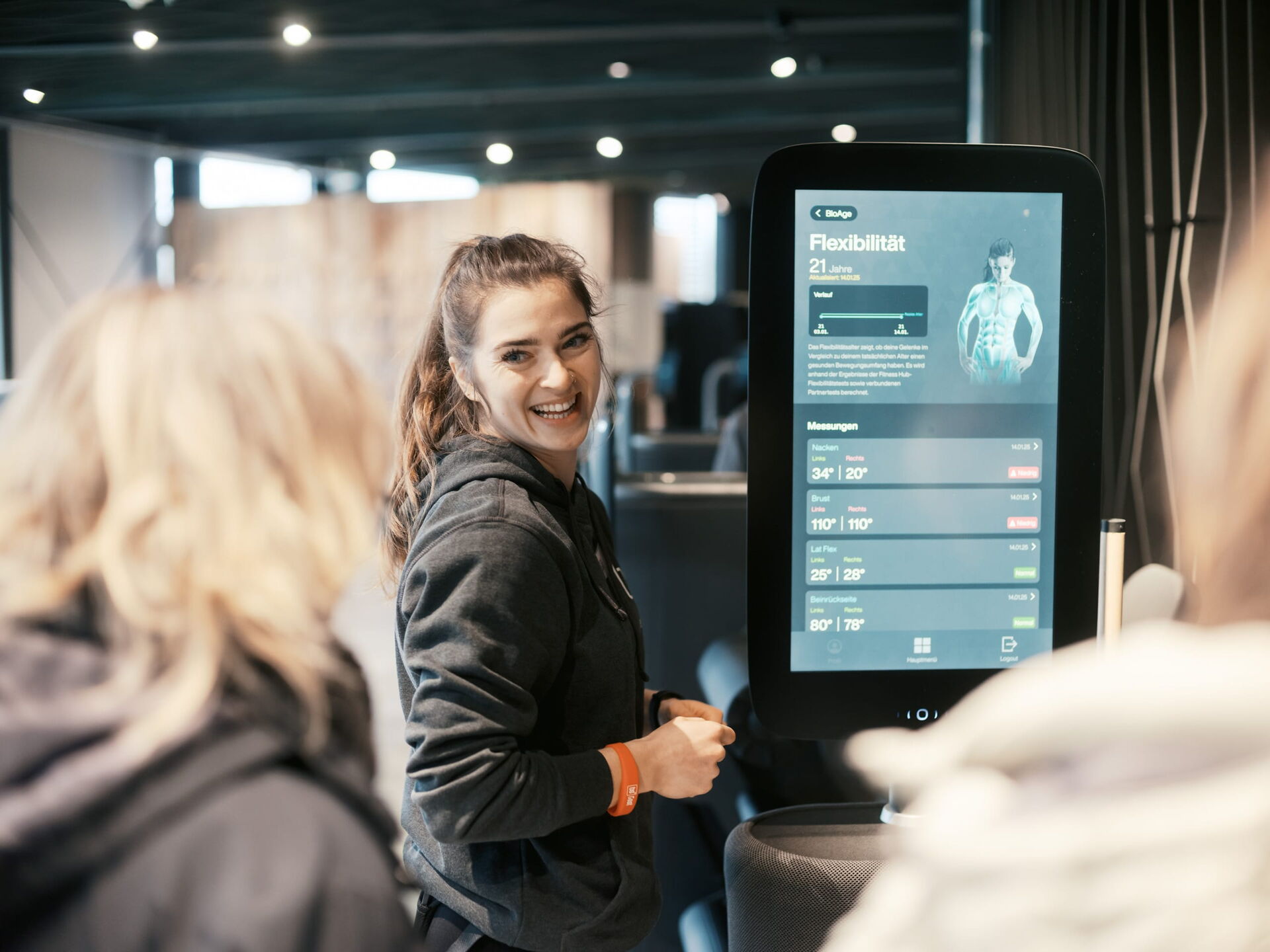 Eine Trainerin lächelt freundlich, während sie an einem digitalen Bildschirm Informationen zur Flexibilität bereitstellt.